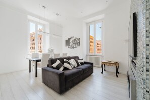 A modern living room with a dark sofa, white walls, and large windows. - Luxury 3 bedroom apartment 4 bathrooms living room and kitchen. (Roma)