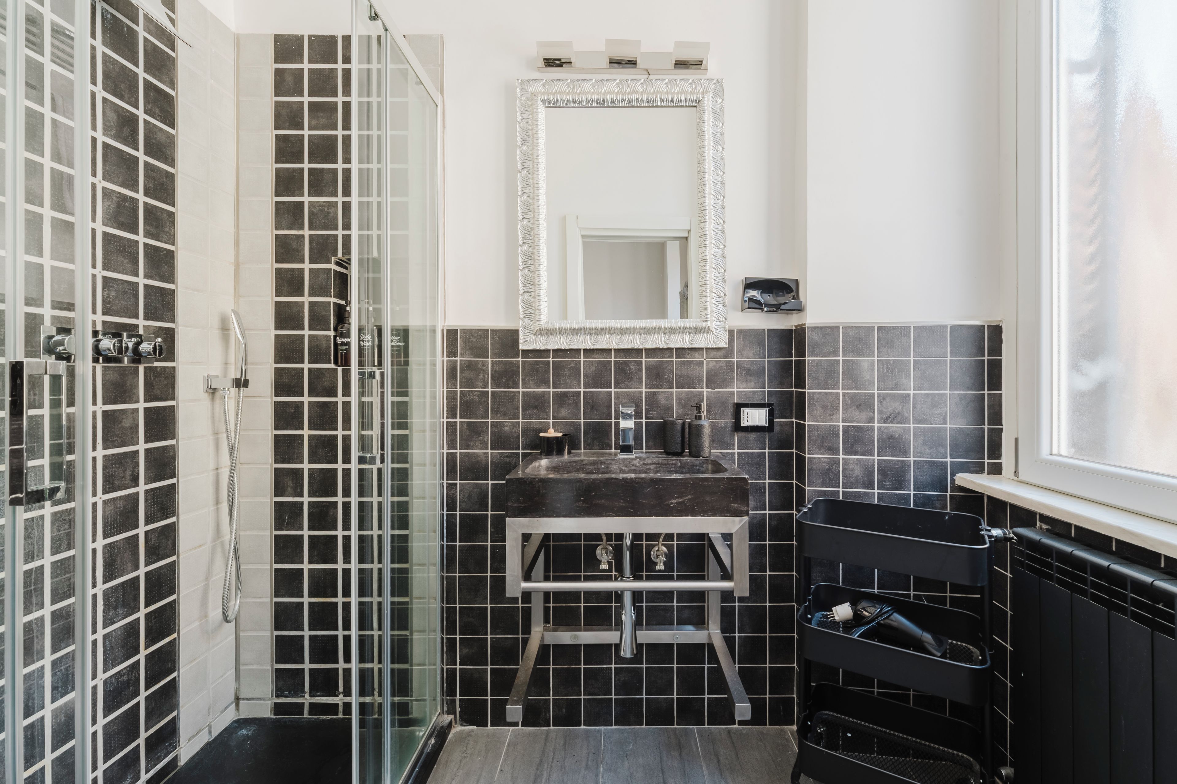 A bathroom with a glass shower enclosure, a sink with a marble countertop, and a black towel rack.