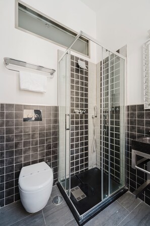 Une salle de bain moderne avec une douche à parois de verre, des toilettes blanches et un sol carrelé de noir.