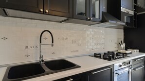 Una cocina moderna con un lavamanos doble, electrodomésticos de acero inoxidable y un salpicadero con baldosas de colores que indican 'BLACK', 'SUGAR', 'WHITE', 'TEA', 'COFFEE', 'MILK' y 'BISCUIT'.