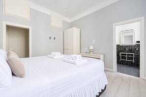 Quarto de hotel com uma cama grande, mesa de cabeceira com abajur, guarda-roupa e banheiro com espelho e azulejos pretos.