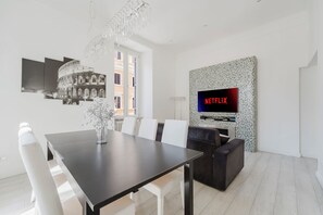 Una sala de estar moderna con comedor, televisor montado en una pared de mosaicos y un candelabro.