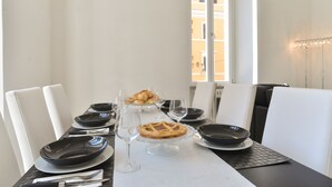 Mesa de comedor preparada para cuatro personas, con platos negros, cristalería transparente y un pastel en un pedestal.