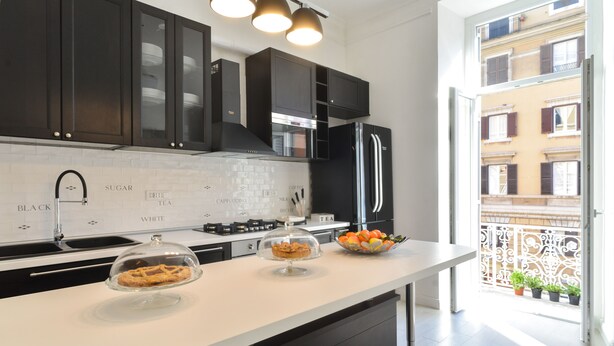 Una cocina moderna con armarios oscuros, una encimera blanca y vistas a un balcón con plantas en macetas.