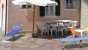 A building with a patio area featuring a table and chairs, a white umbrella, and two lounge chairs.