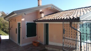 A small house with a tiled roof, a chimney, and a metal gate.