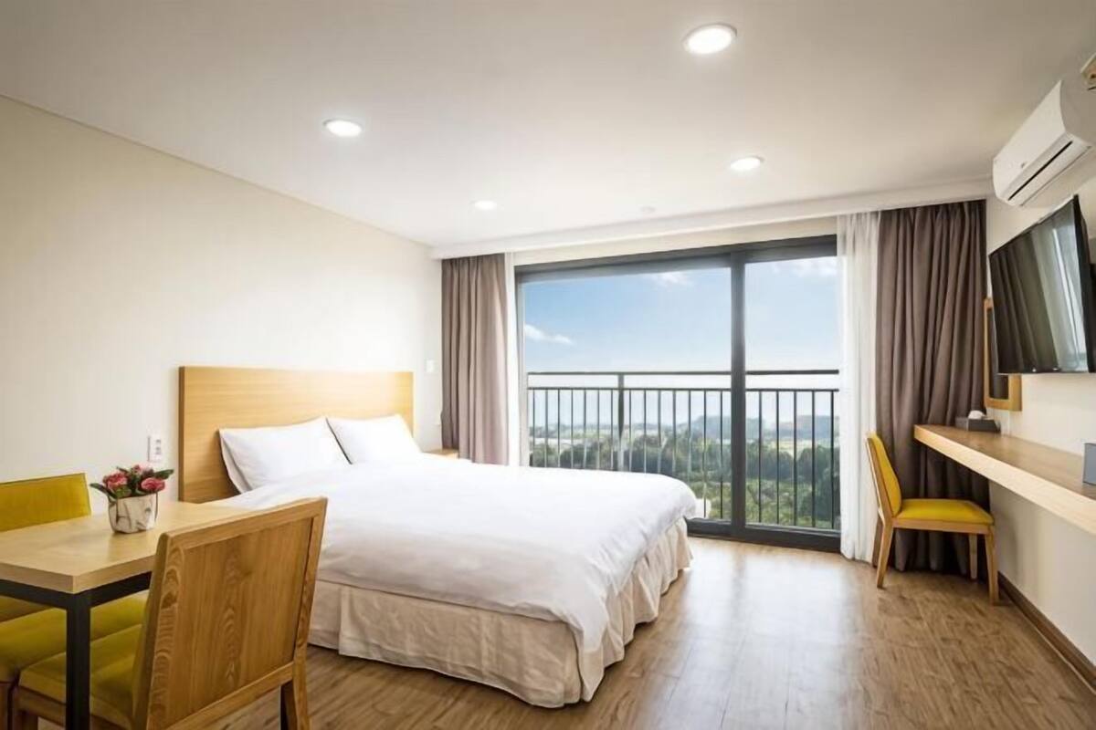 A hotel room with a bed, a desk, a chair, a TV, and a balcony with a view.