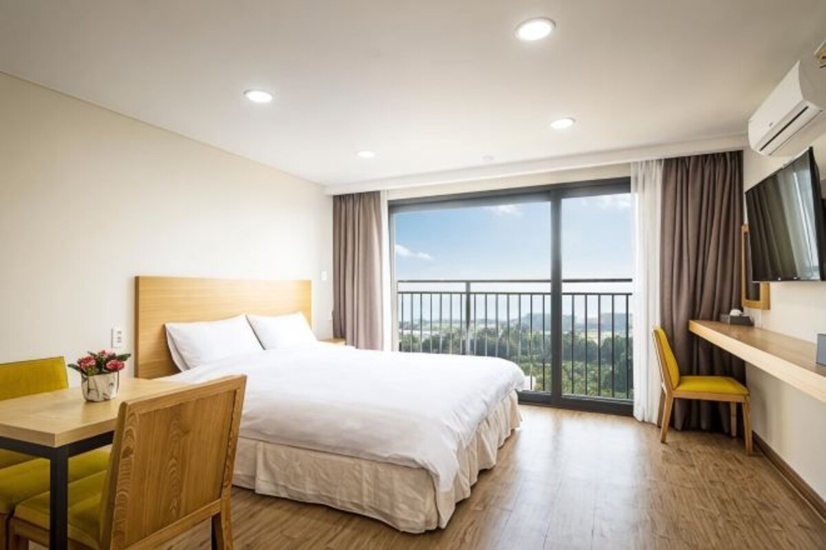 A hotel room with a bed, a desk, a chair, a TV, and a balcony with a view.