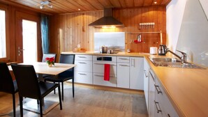 A modern kitchen with wooden paneling, a central island, and a built-in oven. - California House Klosters (Klosters-Serneus)