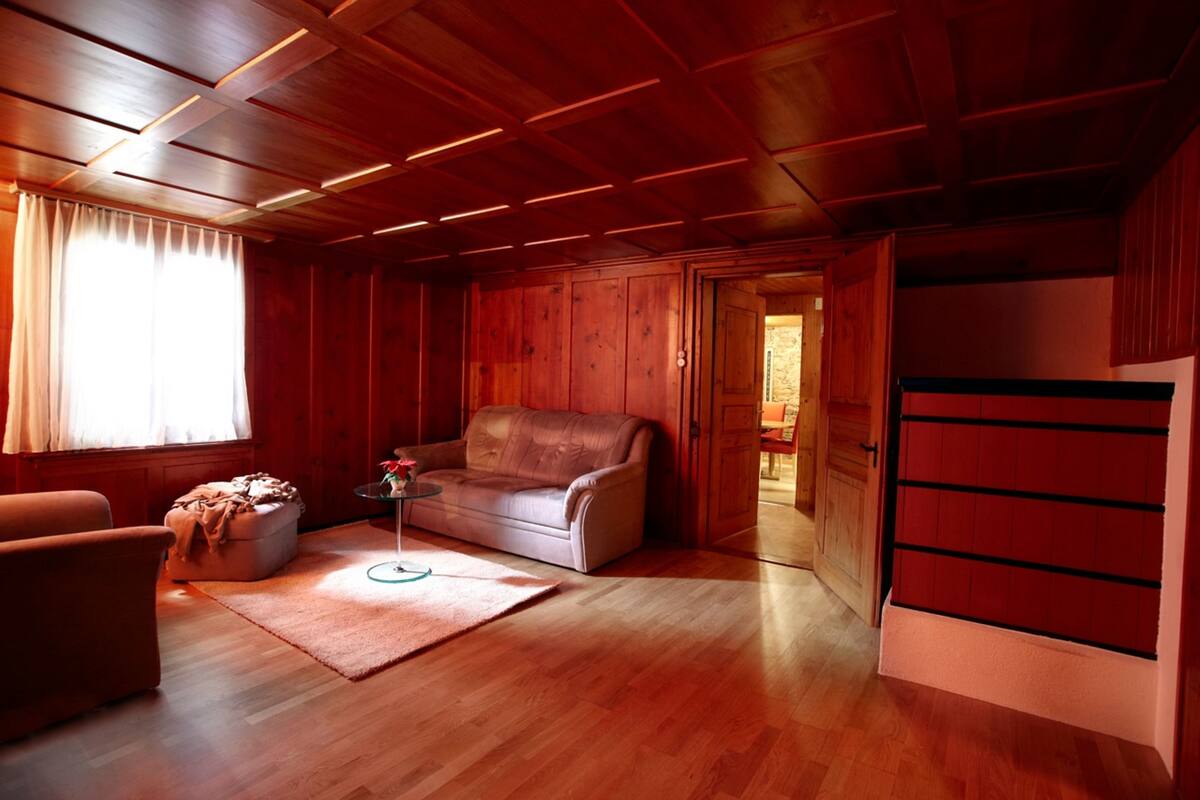 Ein Zimmer mit Holzwänden, einem Ledersofa, einem kleinen runden Tisch und einem Holzschrank.