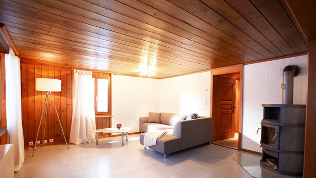 A spacious living room with a wooden ceiling, a sofa, a lamp, and a fireplace. - California House Klosters (Klosters-Serneus)