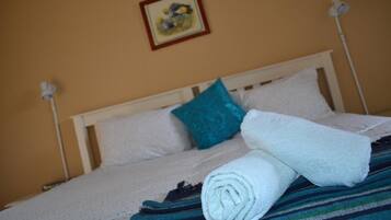 A neatly made bed with white linens, a teal pillow, and a rolled towel on a white headboard.