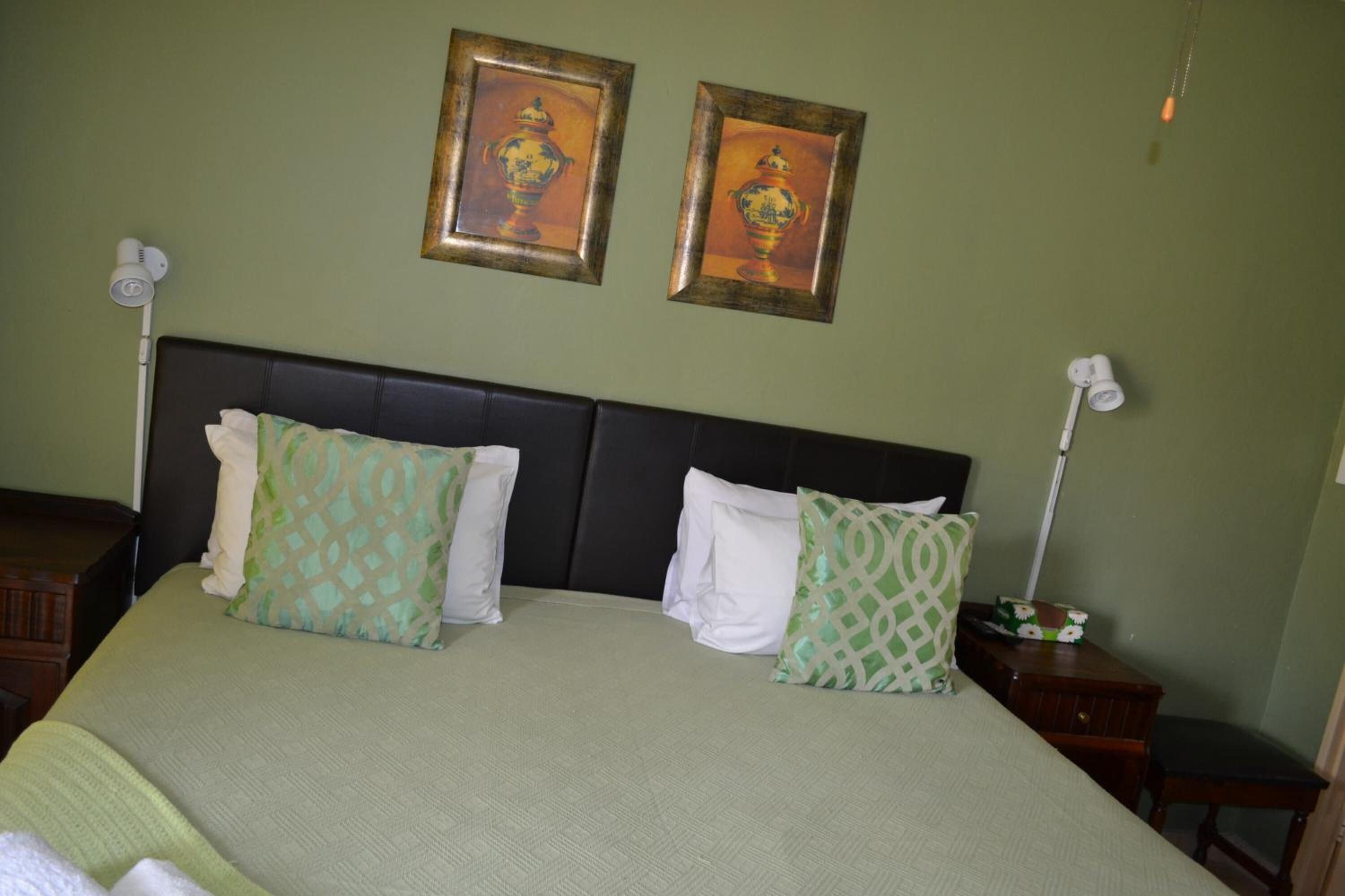A neatly made bed with patterned pillows, a dark headboard, and two wall-mounted lamps.
