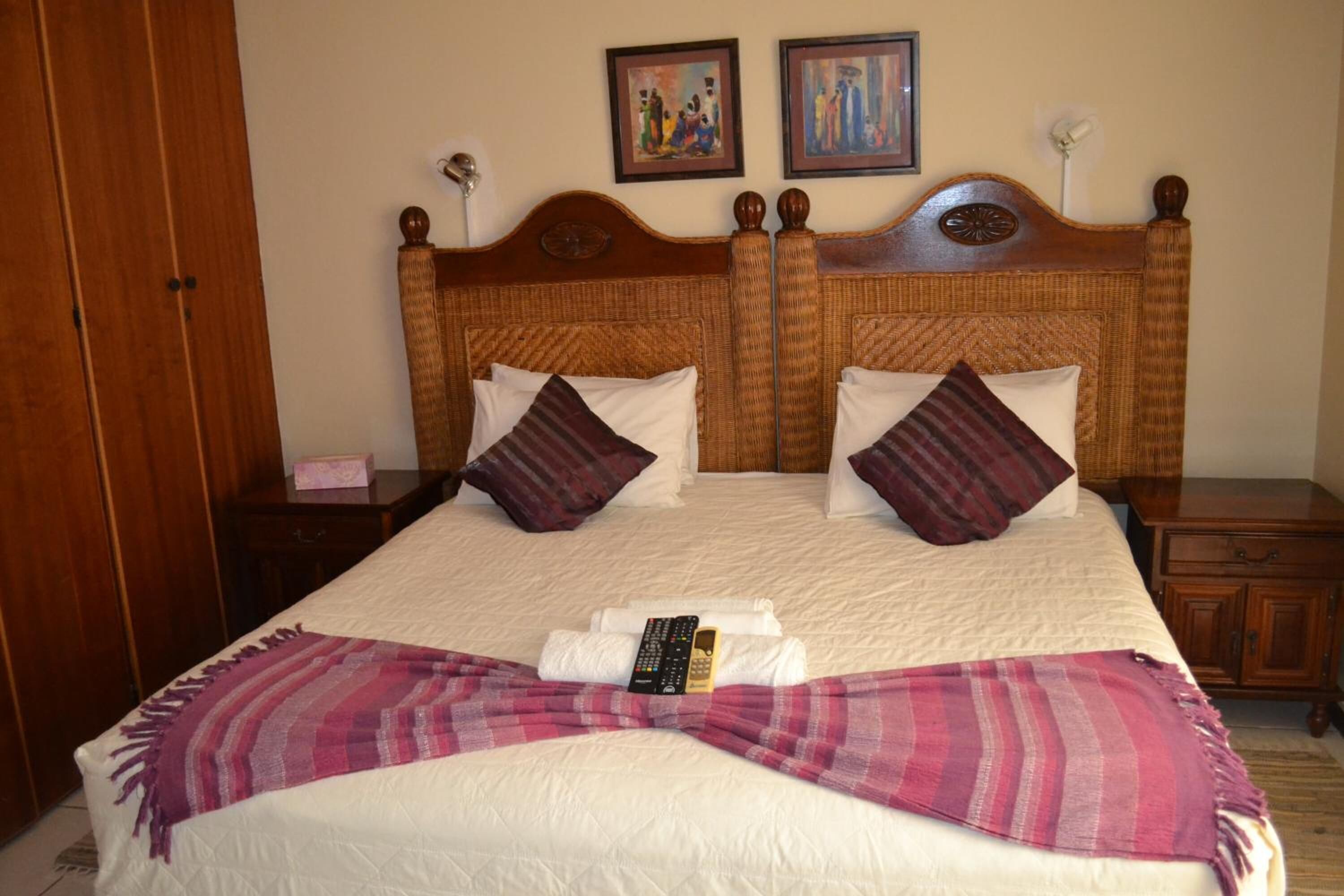 Una cama doble con cabecera de madera, dos almohadas, una colcha y un control remoto sobre la cama.