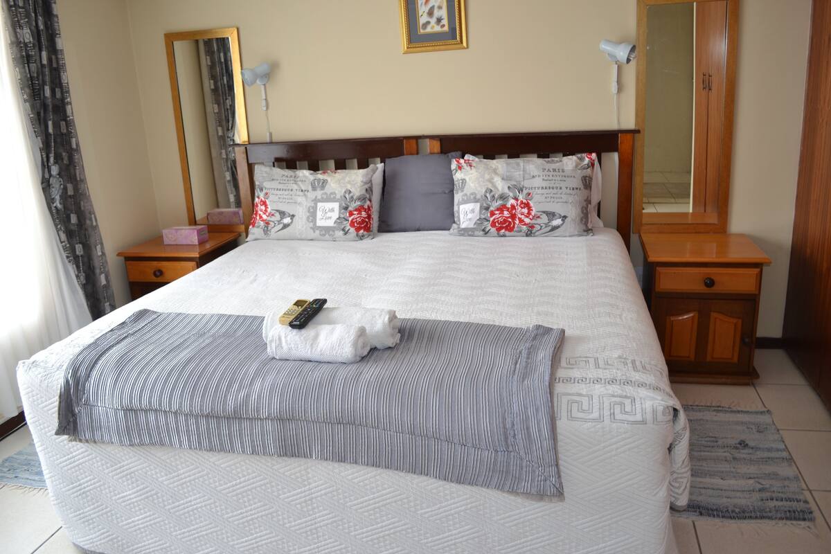 A neatly made bed with a remote control and a folded towel on it. There are two bedside tables with lamps and a mirror on the wall.