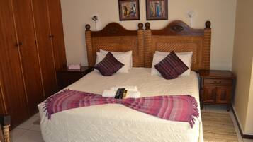 A double bed with a white quilt, two wooden nightstands, a wooden wardrobe, and two paintings on the wall.