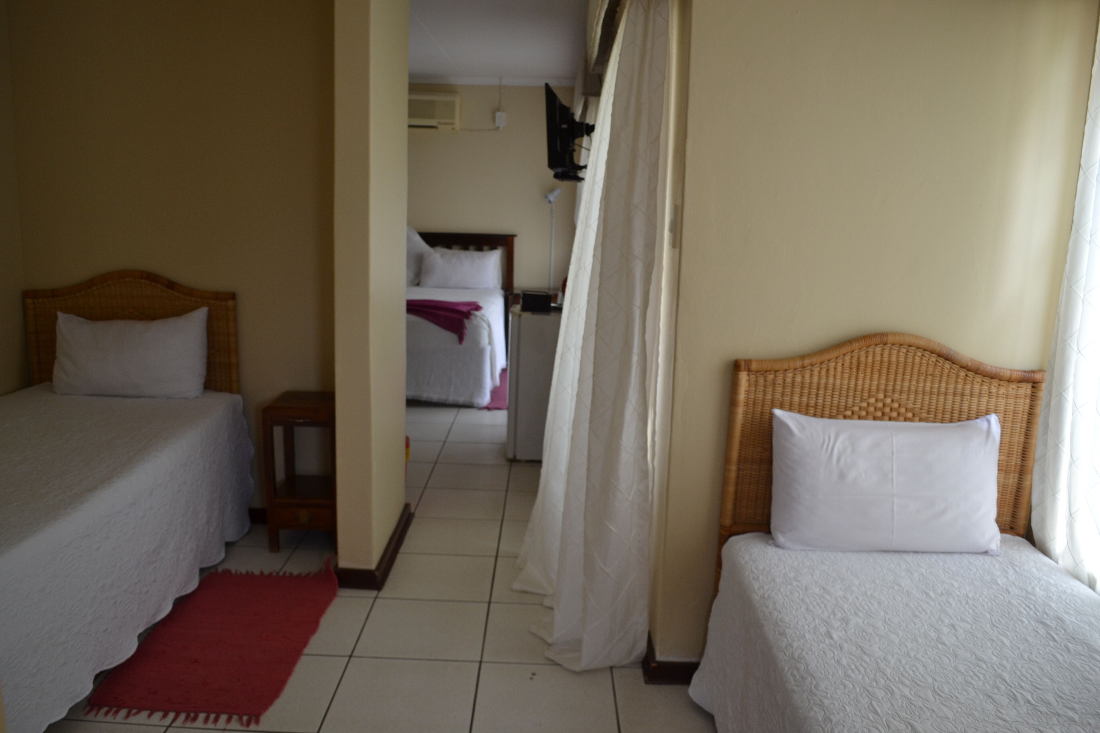Habitación de hotel con dos camas, un tapete rojo y vista a otra habitación.