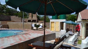 A pool area with lounge chairs, a hot tub, and a covered seating area. - Kamogelo Guest House (Moses Kotane)
