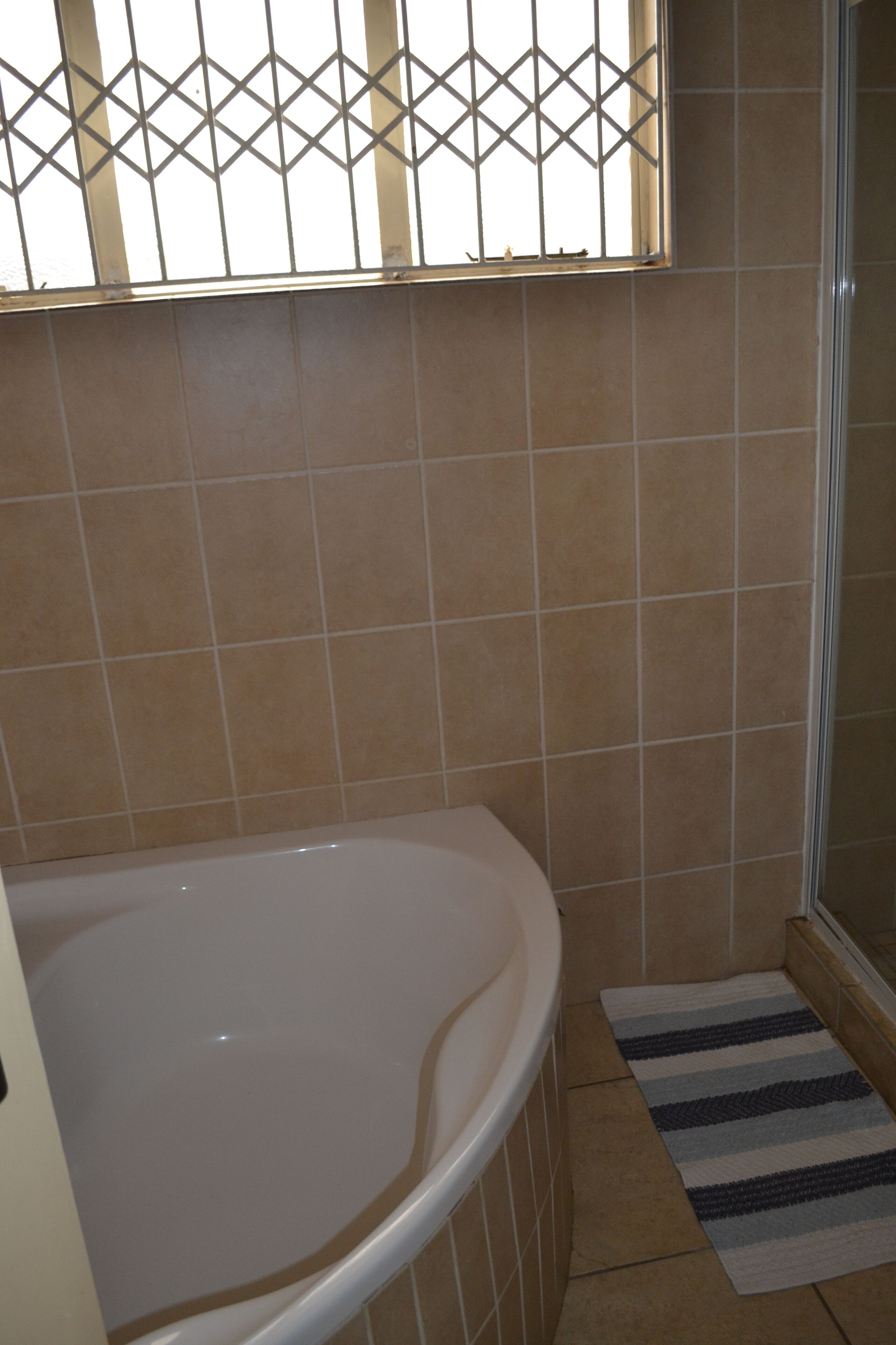 Een badkamer met een bad, een douche en een raam met metalen tralies.
