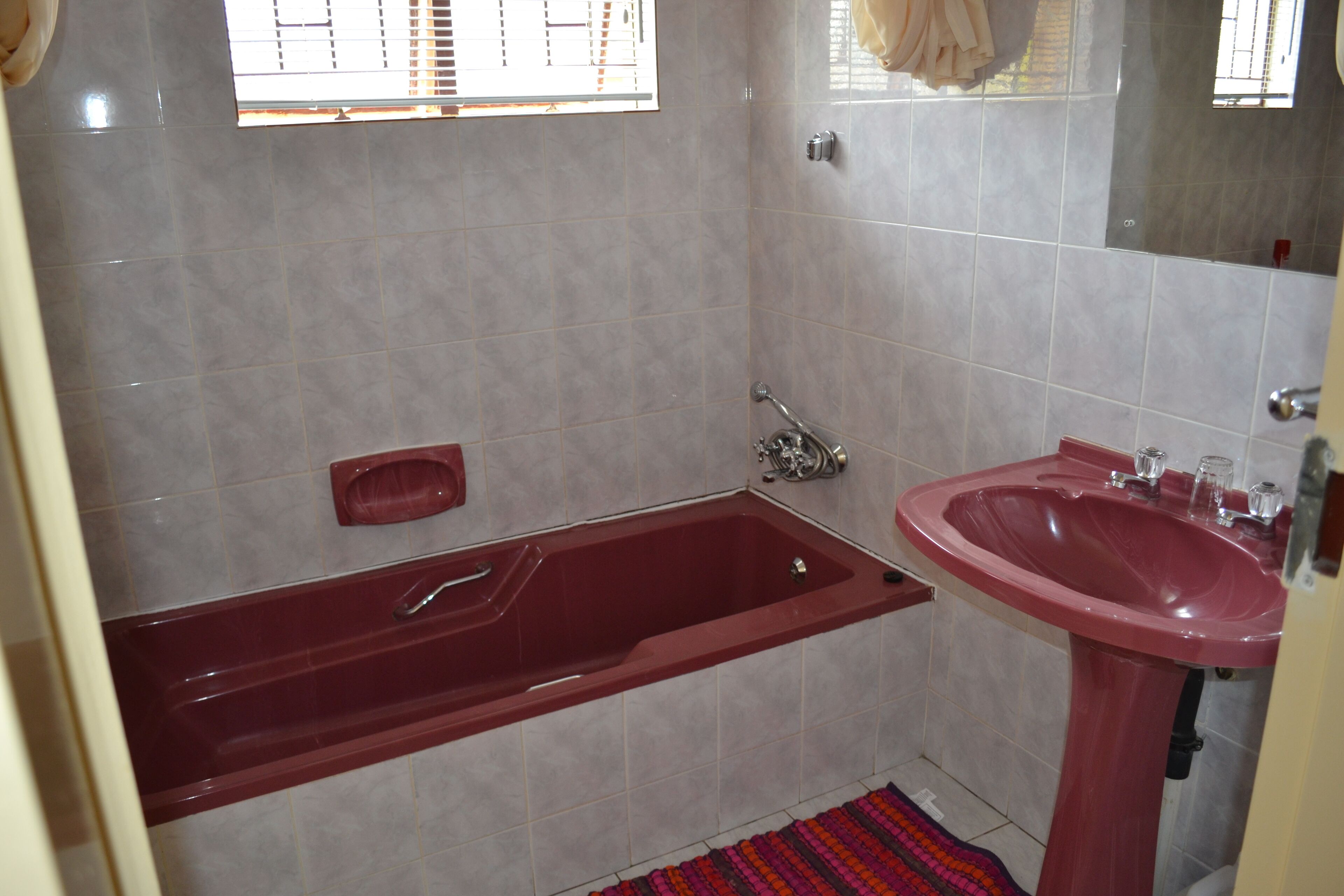 Un baño con una bañera roja, un lavabo y paredes con azulejos.