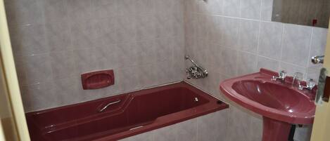 Un baño con una bañera roja, un lavabo y paredes con azulejos.