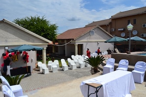 An outdoor event area with white chairs, tables, and umbrellas, a building with a tiled roof, and a clear sky. - Kamogelo Guest House (Moses Kotane)