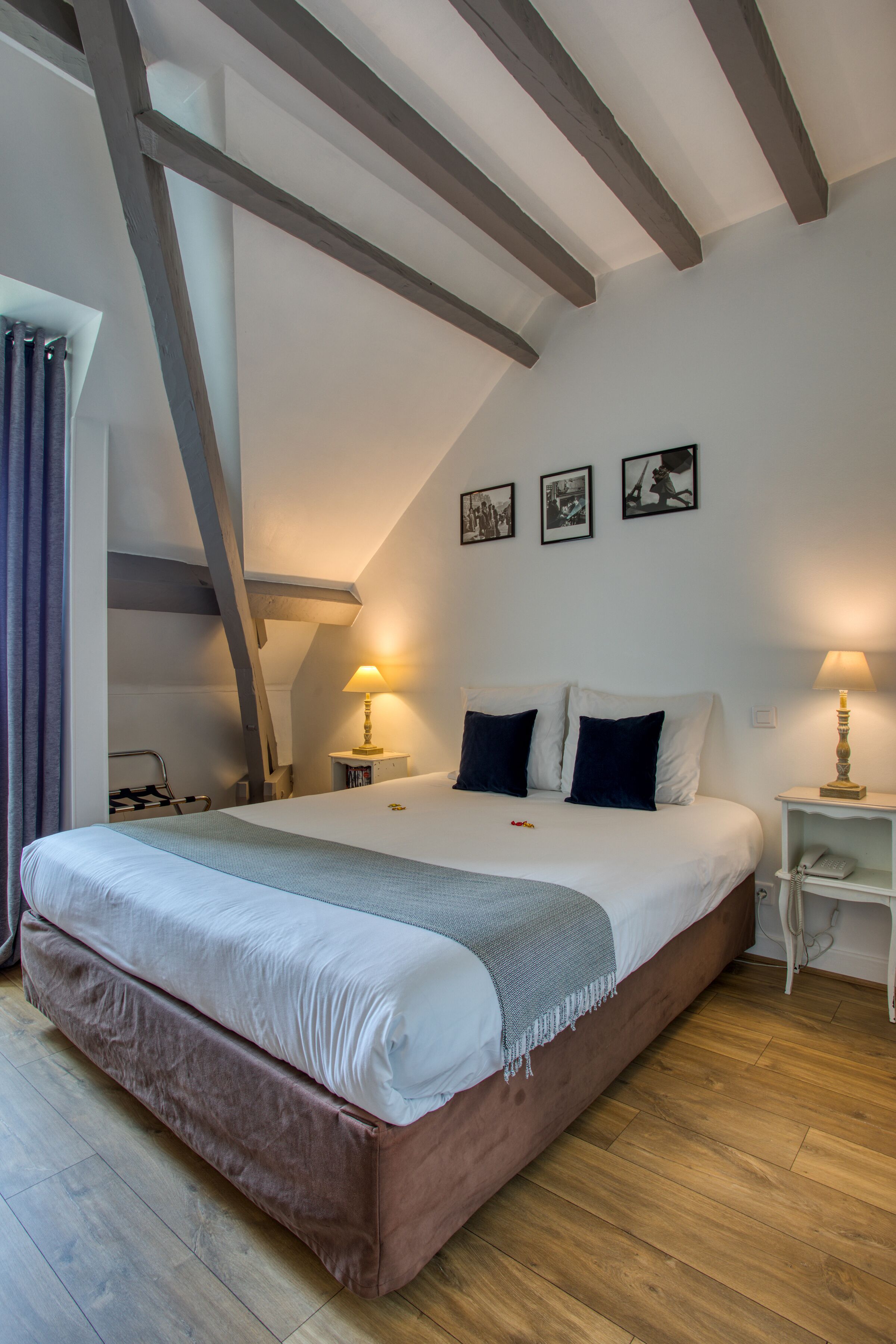 A bedroom with a large bed, wooden beams, a small bedside table, and a nightstand.