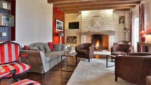 A cozy living room with a fireplace, leather sofas, a striped armchair, and a bookshelf. - Hôtel Restaurant Le Meysset (Sarlat-la-Canéda)