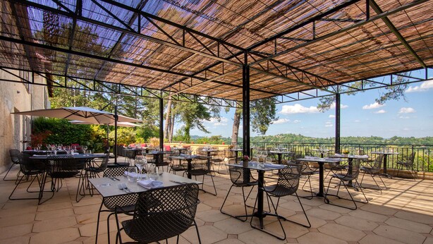 An outdoor patio with hexagonal tables and chairs, a thatched roof, and a scenic view. - Hôtel Restaurant Le Meysset (Sarlat-la-Canéda)