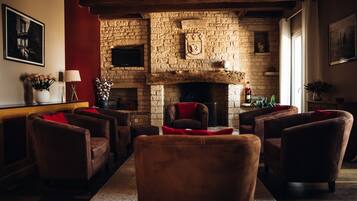 Un salon chaleureux avec une cheminée en pierre, des fauteuils en cuir et un mur d’accent rouge.
