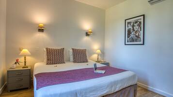 Een netjes opgemaakt bed met een laptop, twee bedlampjes, een ingelijst foto aan de muur, en een klein nachtkastje met een lamp en een vaas.