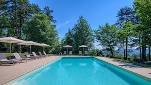 A rectangular swimming pool with clear blue water, surrounded by lounge chairs and umbrellas, set against a backdrop of tall trees and a clear sky. - Hôtel Restaurant Le Meysset (Sarlat-la-Canéda)