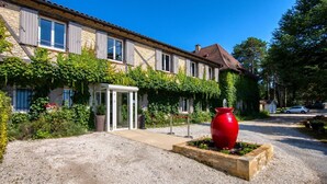 A building with a traditional stone facade, a covered entrance, and a red decorative pot in the foreground. - Hôtel Restaurant Le Meysset (Sarlat-la-Canéda)