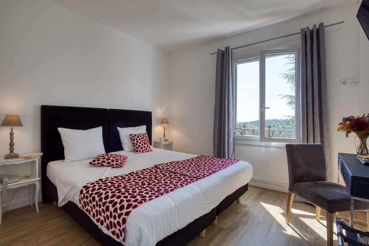 Une chambre à coucher avec un grand lit, des tables de chevet avec des lampes, un bureau avec une chaise et une fenêtre avec des rideaux.