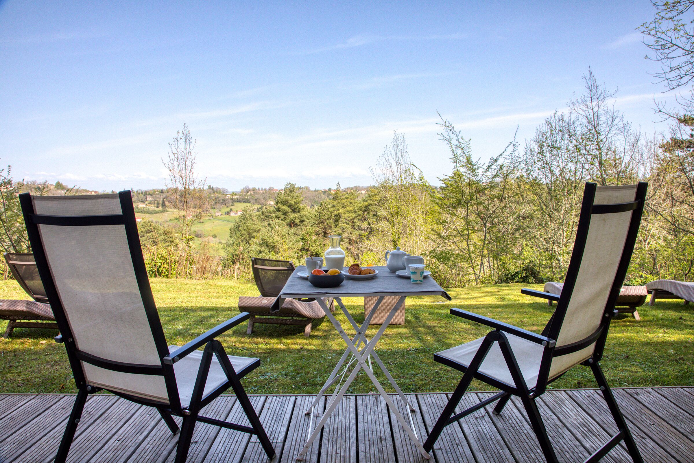 A deck with two chairs and a table set for a meal, overlooking a grassy landscape.