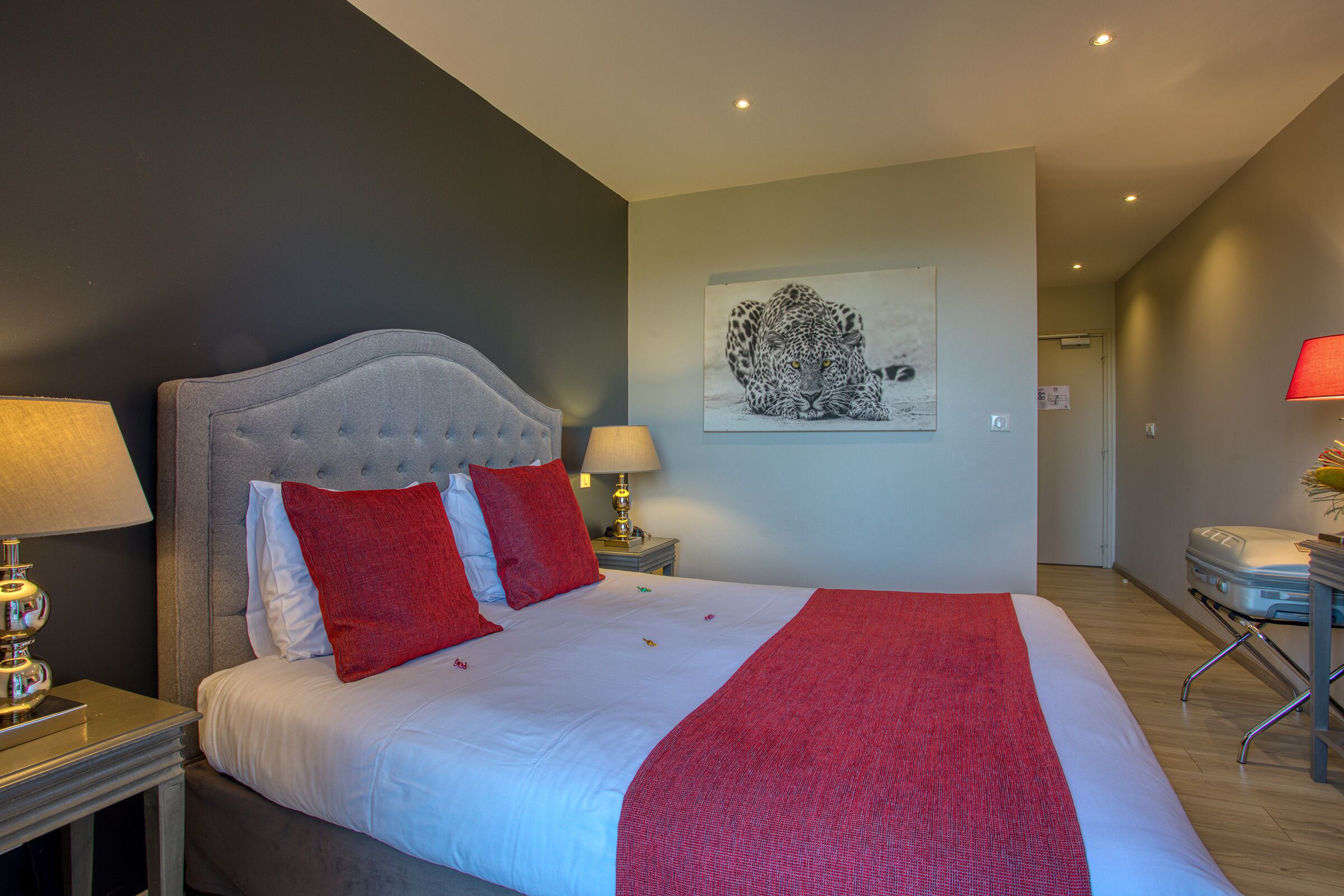 A neatly made bed with red and white bedding, a headboard, and a bedside table with lamps.