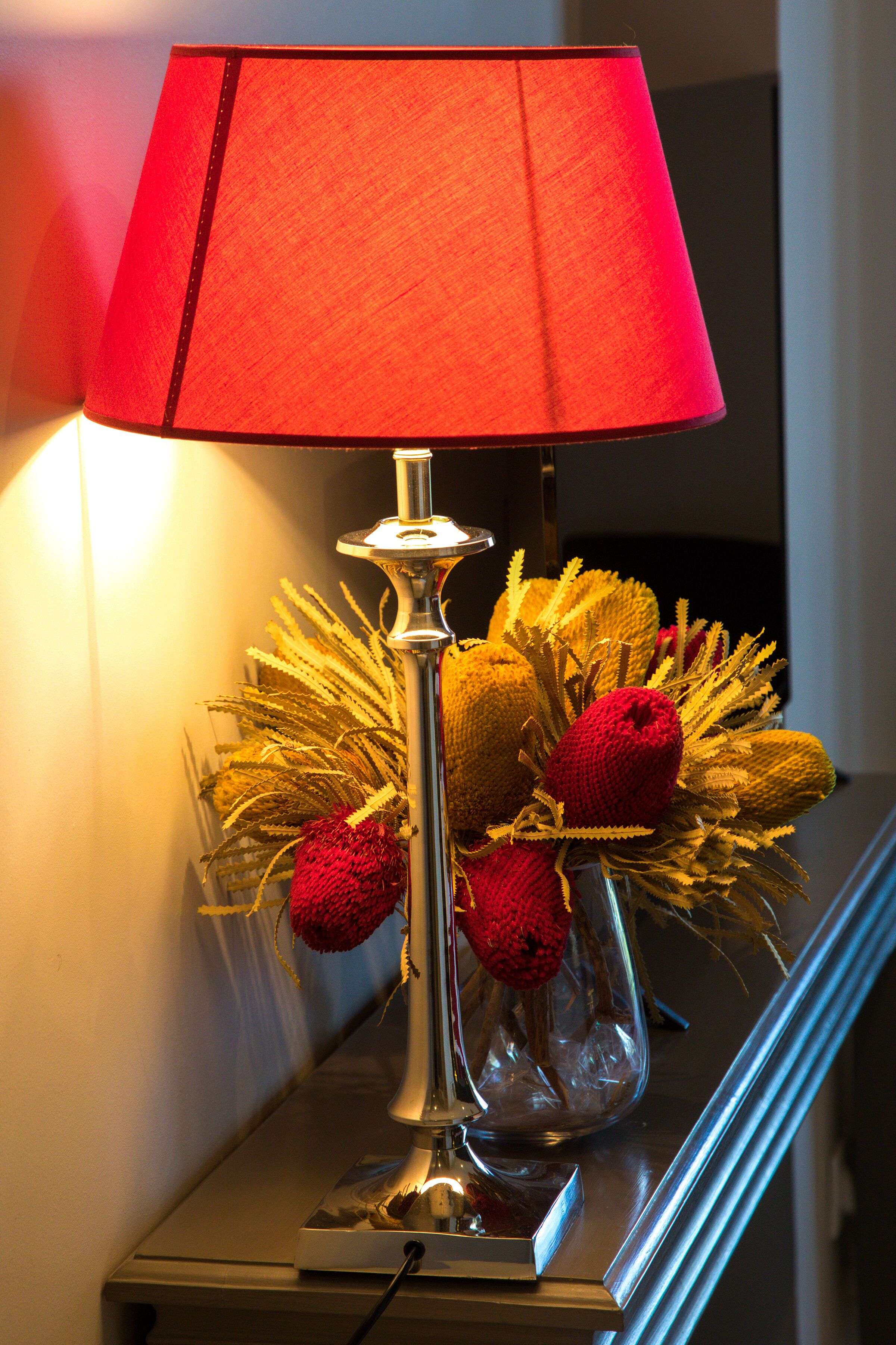 A lamp with a red shade and a vase with golden and red decorative elements on a table.