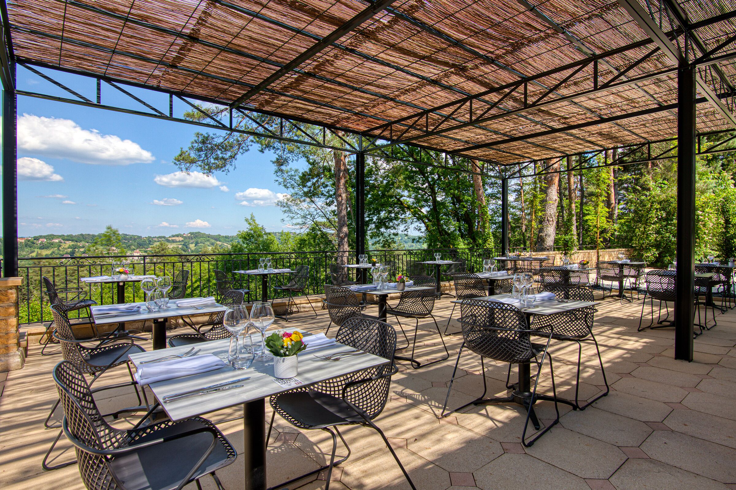 Eine Terrasse im Freien mit Tischen und Stühlen, einer Pergola und Blick auf die umliegende Landschaft.
