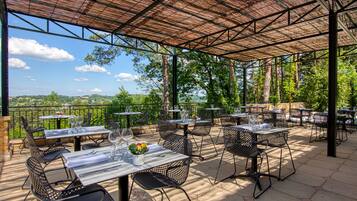 Eine Terrasse im Freien mit Tischen und Stühlen, einer Pergola und Blick auf die umliegende Landschaft.