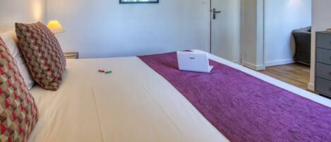 A hotel room with a bed, a laptop, a purple throw, and a framed picture on the wall.