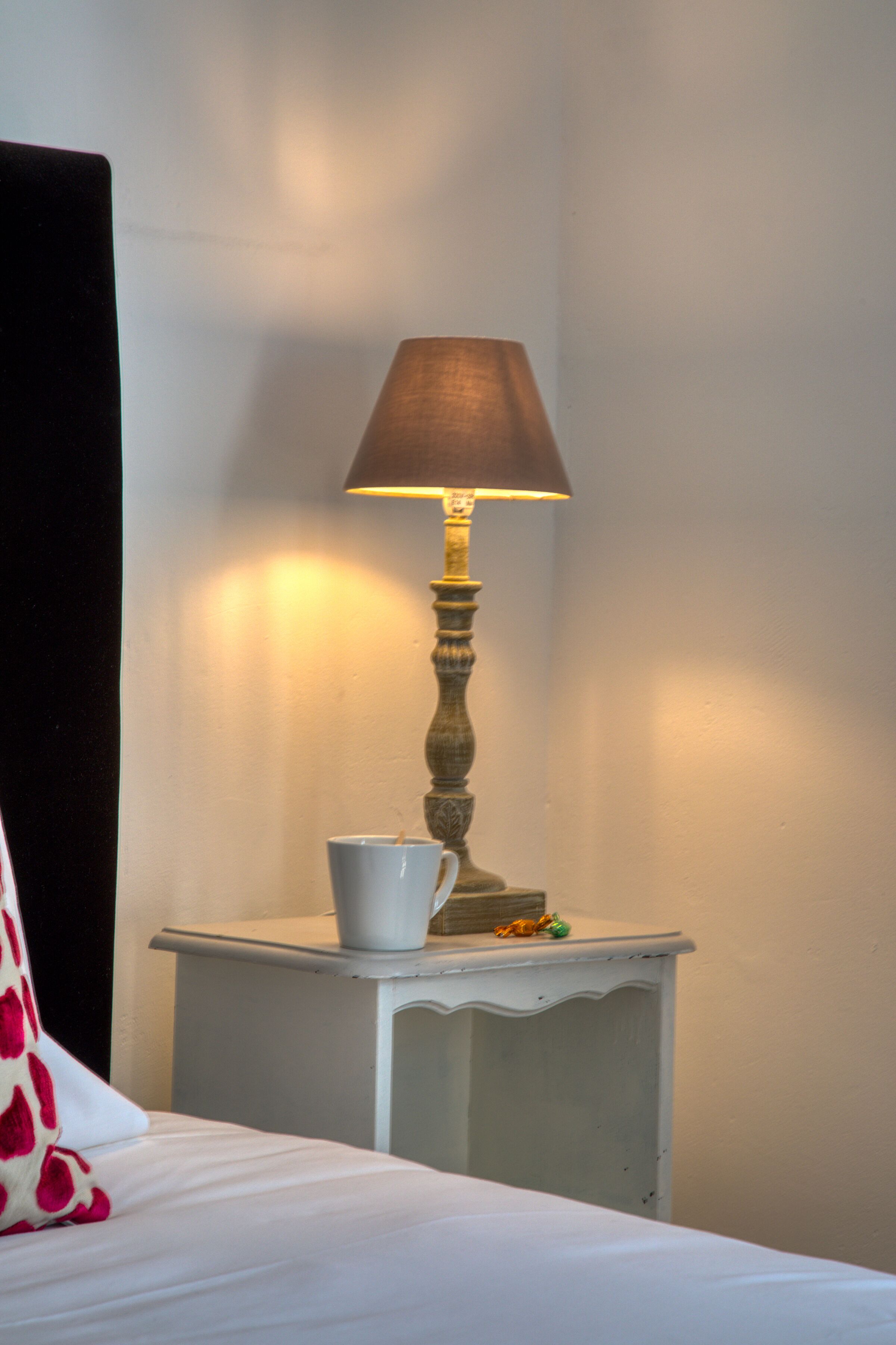 A bedside table with a lamp, a cup, and a decorative item.