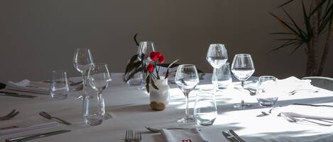 A round dining table with a white tablecloth, set with clear wine glasses, water glasses, and cutlery.