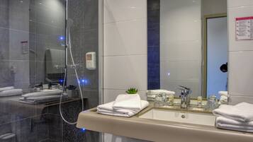 A modern bathroom with a glass-enclosed shower, a large mirror, and a vanity with a sink and towel rack.