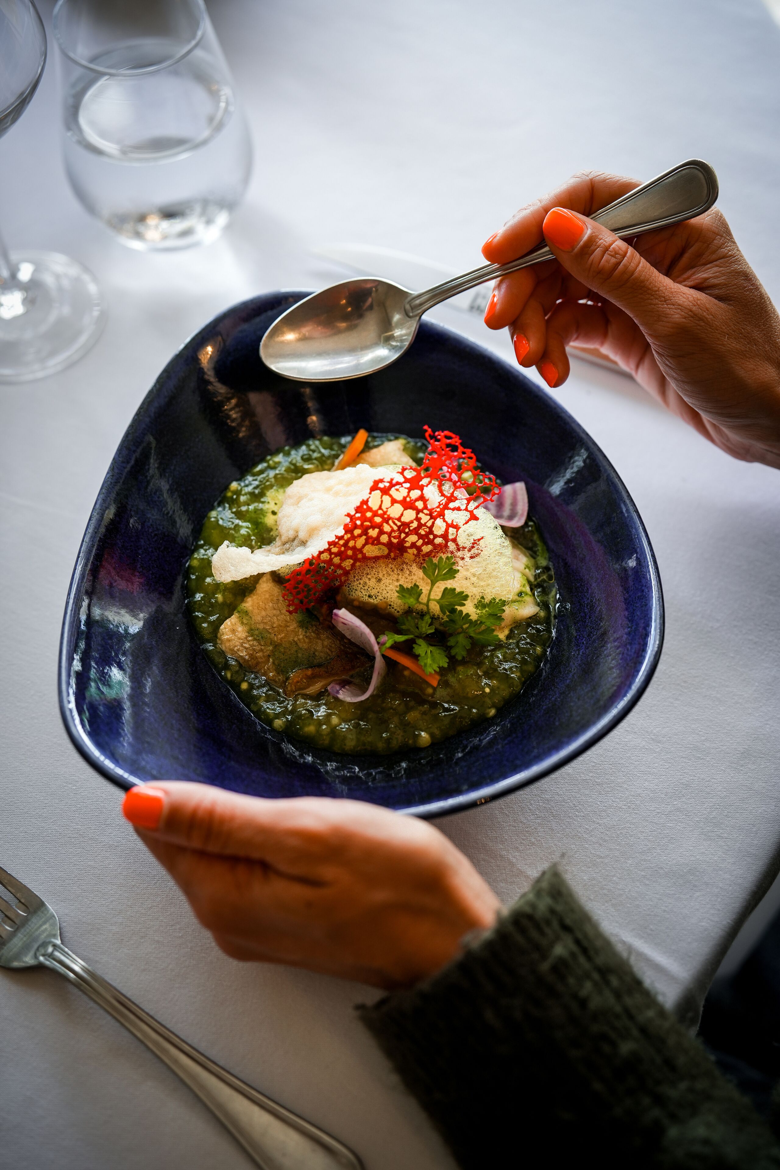 A person holding a spoon over a bowl of food with a blue rim.
