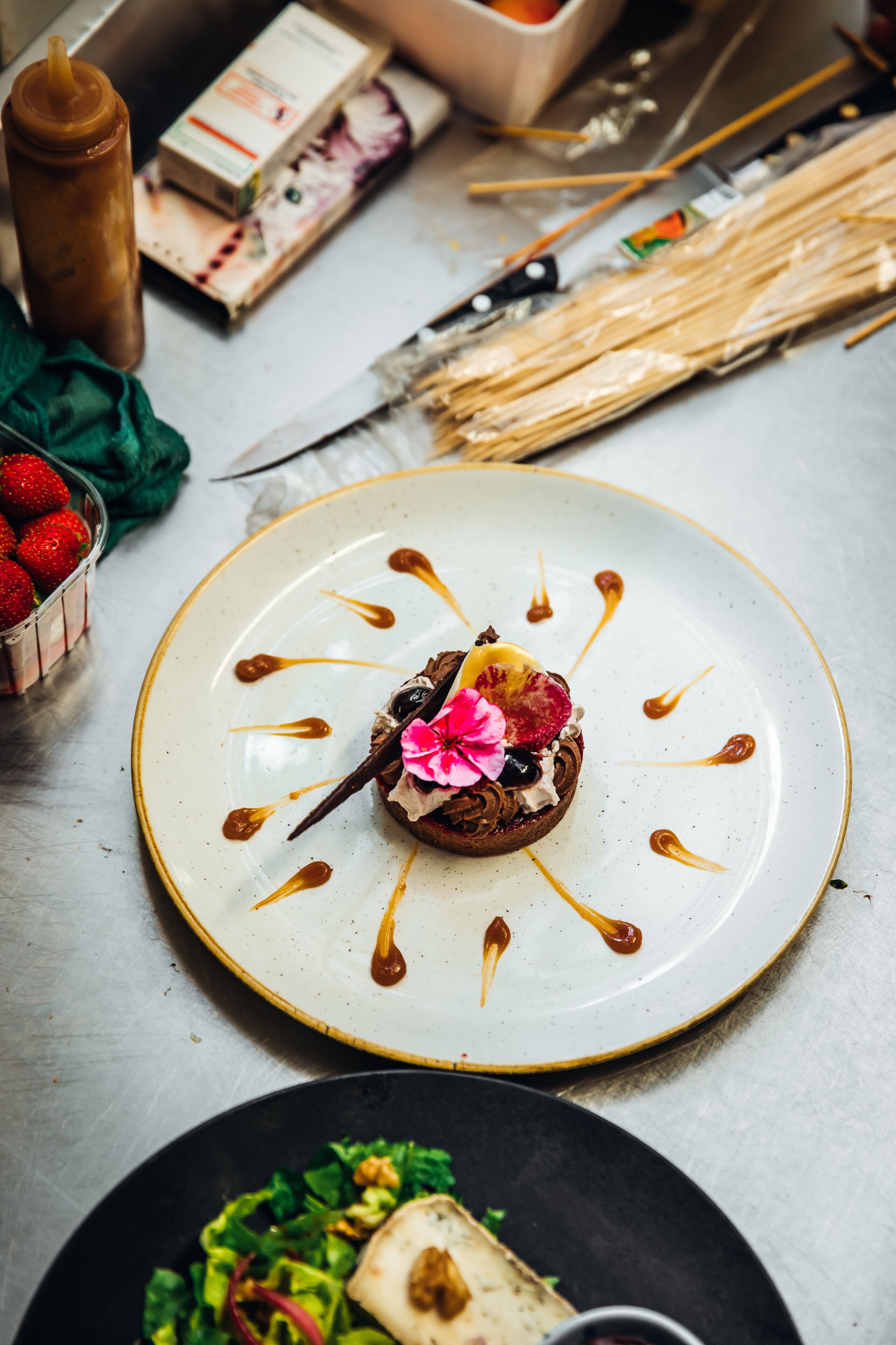 A dessert on a plate with drizzled sauce, a bowl of strawberries, and a knife on a table.