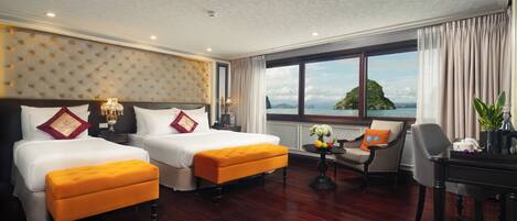 A hotel room with two beds, a sitting area with a chair and table, and a large window with a view of the sea.