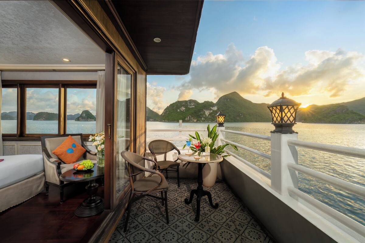 A balcony with a table, chairs, and a view of the sea and mountains.