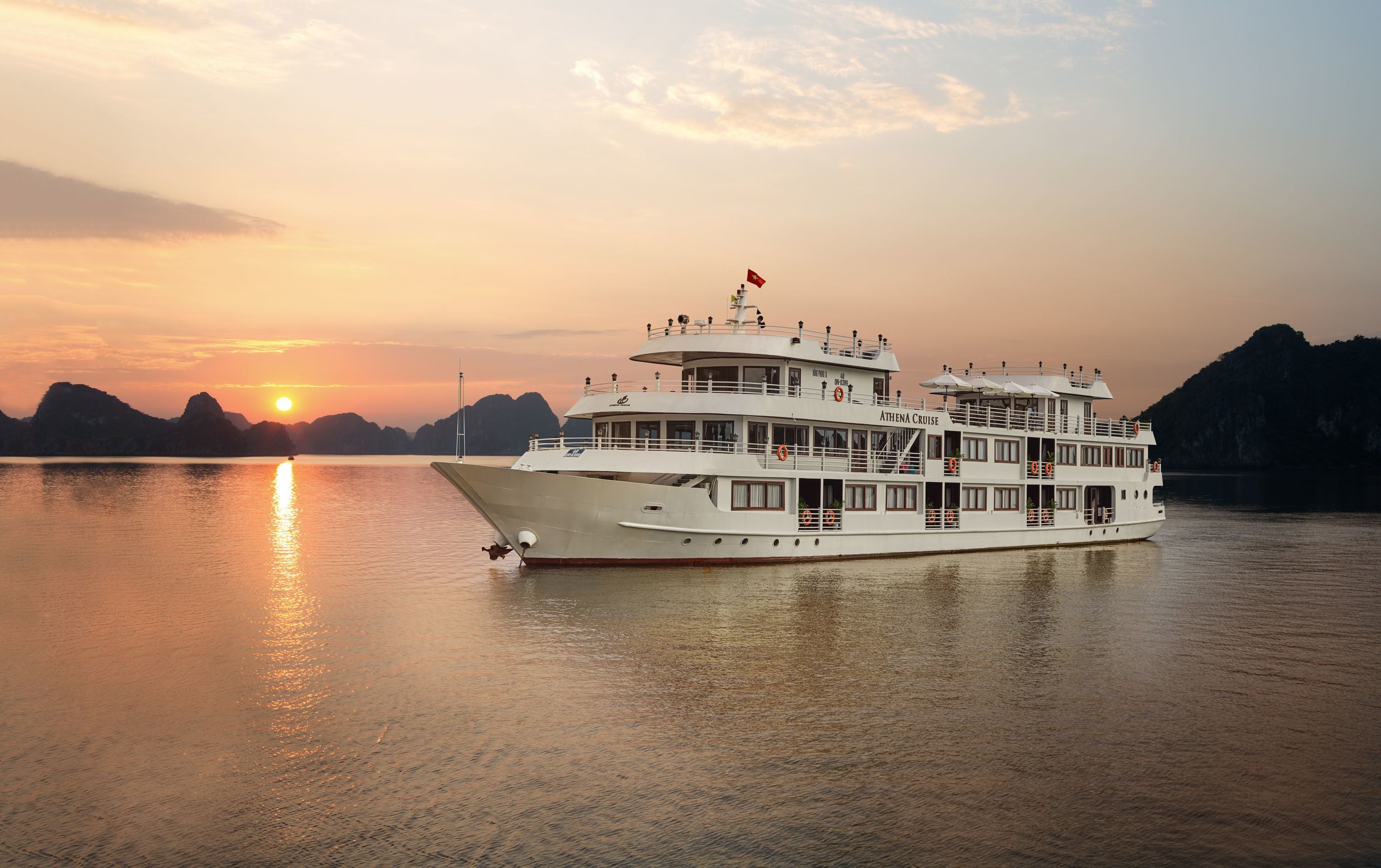 A white cruise ship named ATHENA CRUISE sailing on calm waters during sunset.