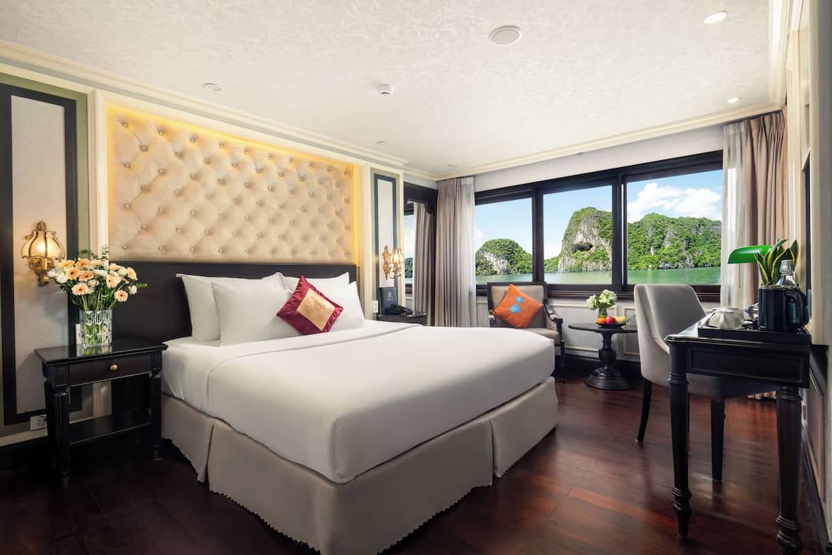 A spacious hotel room with a large bed, a desk, and a view of the sea.