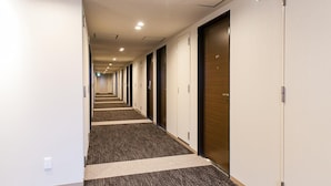 A hotel hallway with carpeted floors, white walls, and doors with numbers. - Y’s Hotel Shin - Osaka (Osaka)